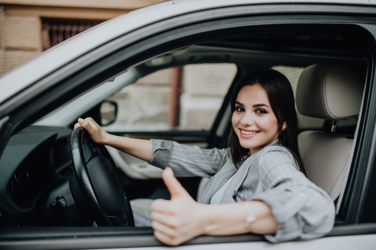 Young woman sitting in the car and showing thumbs up